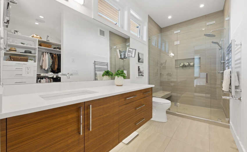 Floating Walnut cabinetry and quartz countertops in this gorgeous ensuite with a reflection of the walk in closet.  Under cabinet illumination.